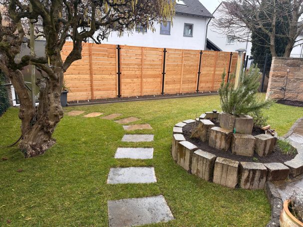 Ein Garten mit einem Steg, einer Steinmauer und einer kleinen Wasserstelle.